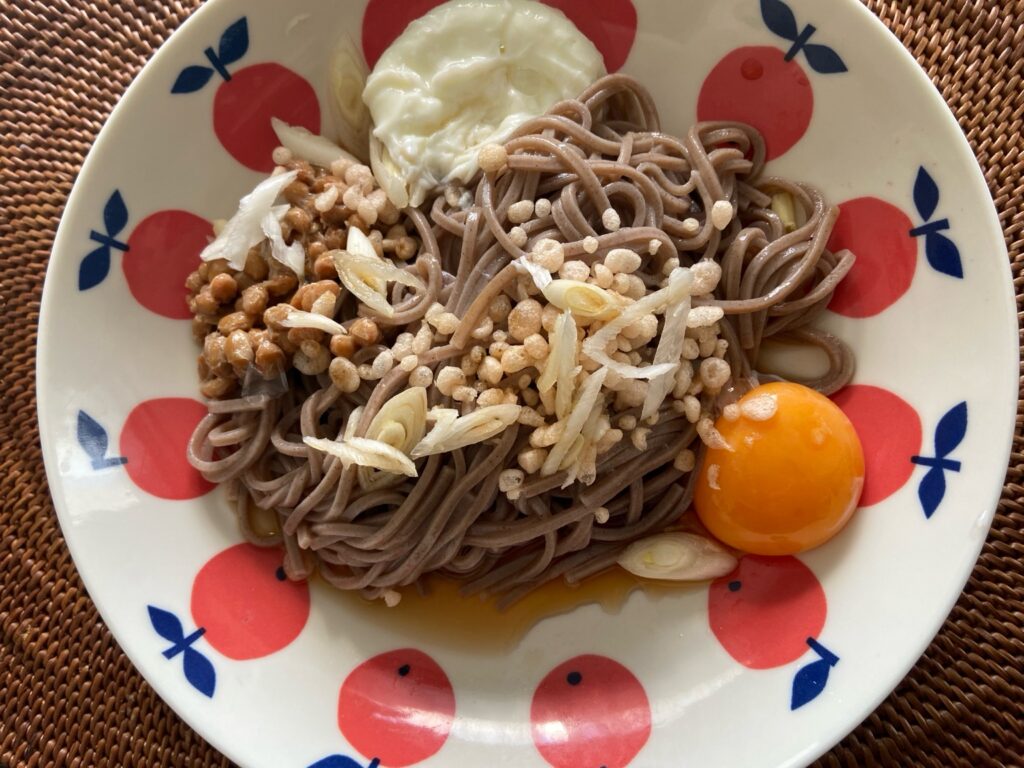 Japanese tanuki soba noodles served in a decorative bowl, garnished with tempura bits, egg yolk, and green onions.