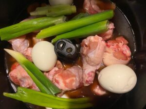 Chicken drumsticks, boiled eggs, and green onions in a vinegar-based sauce prepared in an auto cooker. 