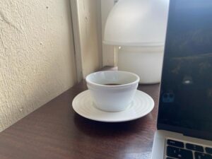 A white coffee cup on a wooden table next to a laptop in a serene cafe.