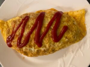 A Japanese omelette rice dish, served on a white plate, topped with a zigzag of ketchup.