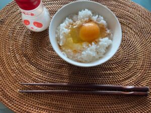 Tamago Kake Gohan (rice with raw egg yolk) served in a bowl with chopsticks and soy sauce bottle on a woven placemat.