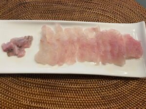 Slices of flounder sashimi arranged on a white plate with a woven placemat background.