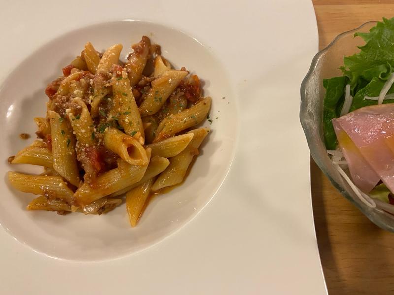 A plate of penne arrabbiata with a rich tomato sauce and a side salad with ham and fresh vegetables.