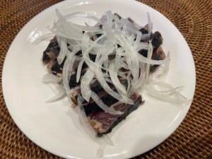 Seared bonito slices with sliced onions on a white plate against a woven placemat.