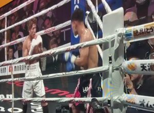 Boxing match scene on TV, showing two fighters in the ring with an audience in the background.